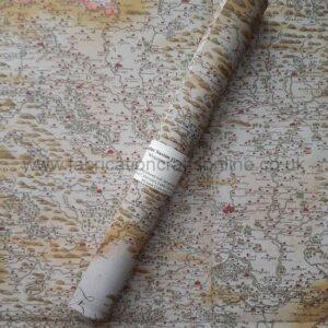 A roll of paper printed with a copy of a hand printed and hand painted map in greens, browns, and yellows, with towns painted red lying on top of an open sheet of the same paper.