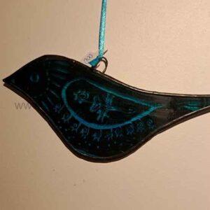 A dark decorative bird-shaped ornament hangs from a blue ribbon against a plain background. The bird features blue accents and intricate floral and symbolic patterns across its body
