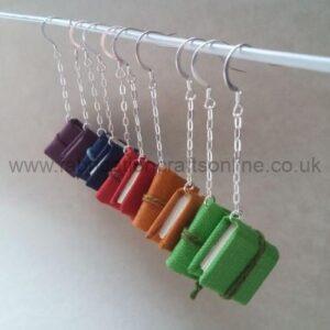 Five differently coloured pairs of book earrings hanging from silver chains and earhooks.