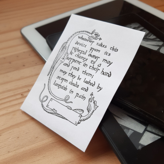 A bookplate sticker with text and two dragons on leaned up against some digital tablets.