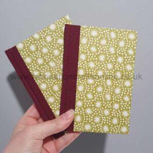 A hand holding a couple of notebooks with book cloth spines and decorative paper covers.