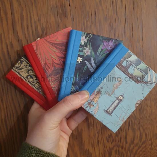 A hand holding four books all A7 in size. Two have red spines, two blue, and each has a different decorative paper on the cover