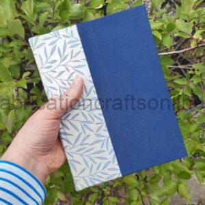 A hand holding a book with blue willow pattern spine and solid blue book cloth on the covers.
