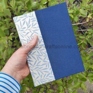 A hand holding a book with blue willow pattern spine and solid blue book cloth on the covers.