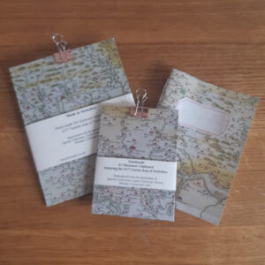 Two clipboards and a notebook all with the same historic map pattern printed on them.
