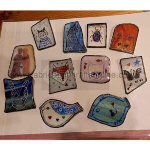 glass brooches Twelve small hand‑painted ceramic or enamel pins are arranged on a flat surface. Each piece features a different colourful illustration, including stylised cats, birds, a fox, a beetle, squirrels, and several abstract or whimsical faces. The designs mix bold outlines with playful shapes and patterns, creating a lively, eclectic set of miniature artworks.
