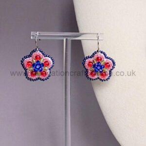 Beaded flower-shaped earrings on a metal stand, featuring blue centers and pink petals with dark blue edges.
