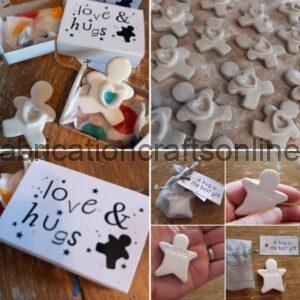 Gift set with white ceramic star/angel shapes and a box reading 'love & hugs' on a wooden table, some pieces inside the box and others outside.
