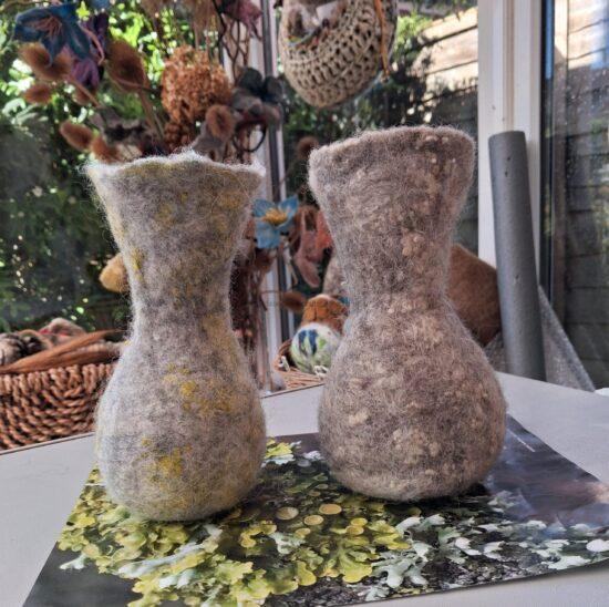 Two fuzzy, felted plant pots sit on a glossy table, with dried botanicals and a wicker basket blurred in the background.