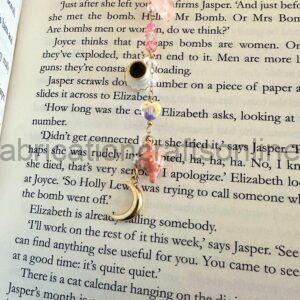 Bracelet with pink beads and a small shell pendant drapes over an open book page with printed text.