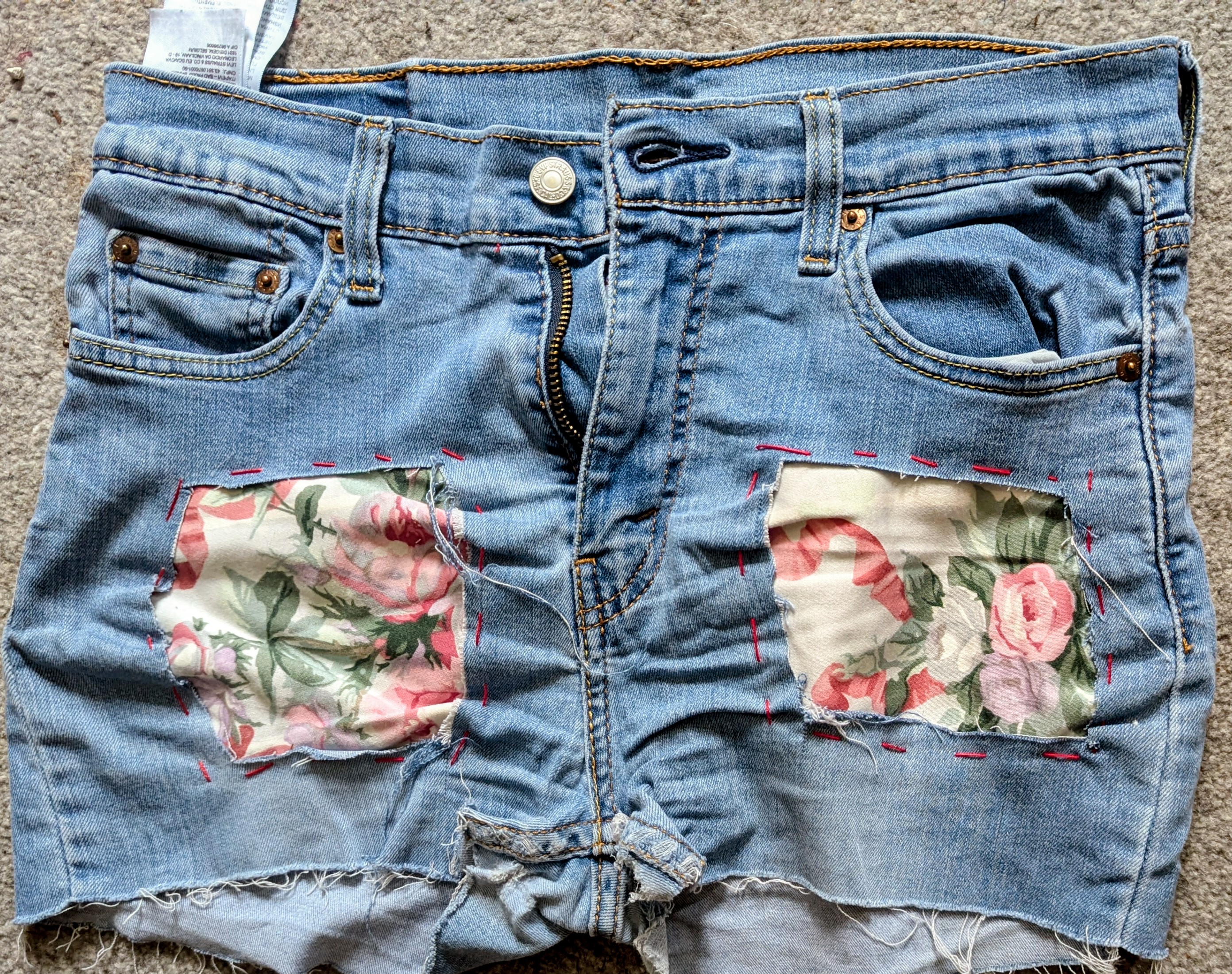 Light blue denim shorts with frayed hems and floral fabric patches sewn over the pockets and leg areas.
