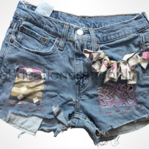 Upcycled denim shorts with patchwork squares and a fabric bow on the right leg.
