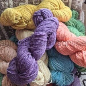 Assorted skeins of soft yarn in pastel and bright colors piled together on a patterned surface.