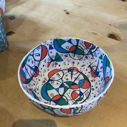Colorful abstract-patterned paper bowl on a wooden table edge visible in the foreground.