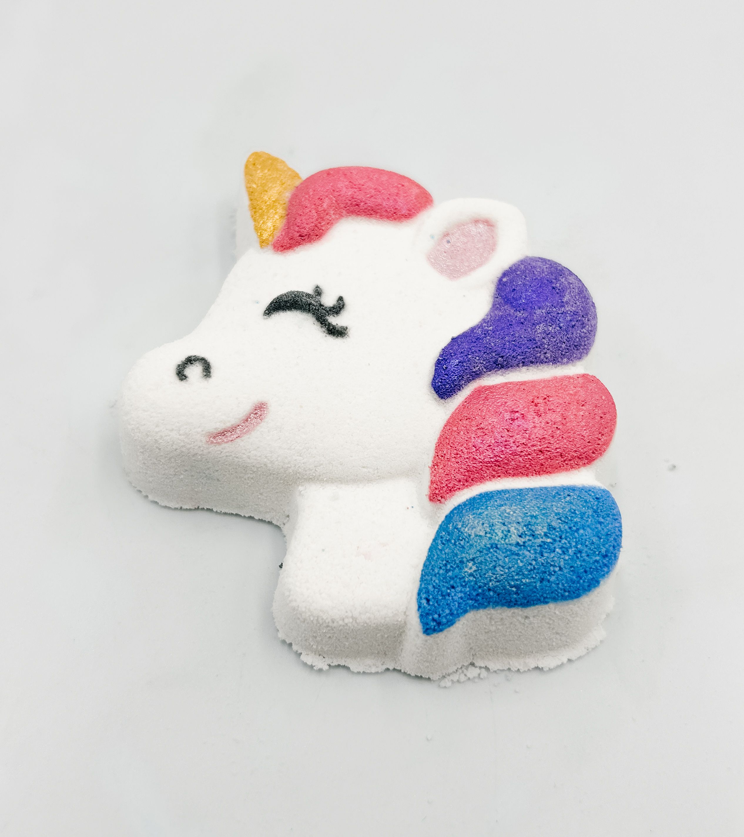 Close-up of a white unicorn figure with a golden horn and rainbow mane made of grainy, sugary crystals