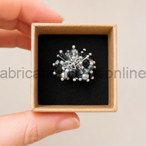 Small jewelry brooch with silver and black beads in a black foam-lined gift box, held by fingertips for display