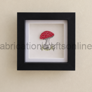 Framed artwork of a red mushroom with white spots on a beige wall, black frame, small sketchy grass at base.
