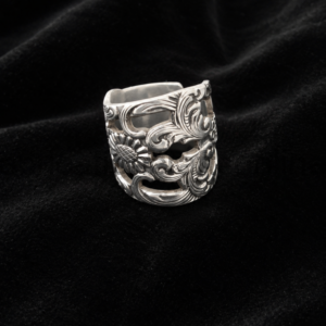 Intricately engraved silver ring with floral and scrollwork patterns on a black velvet backdrop.