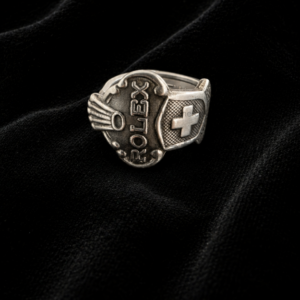 Silver signet ring with a heart-shaped face bearing the word FLEX and a wing motif on dark fabric.