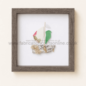 Textile art framed in a dark wood square frame: a small sailboat collage on white background built from fabric scraps and rope pieces.