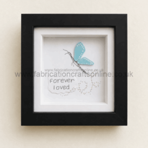 Framed artwork with a blue butterfly perched above the handwritten words ‘Forever I loved’ on white paper.