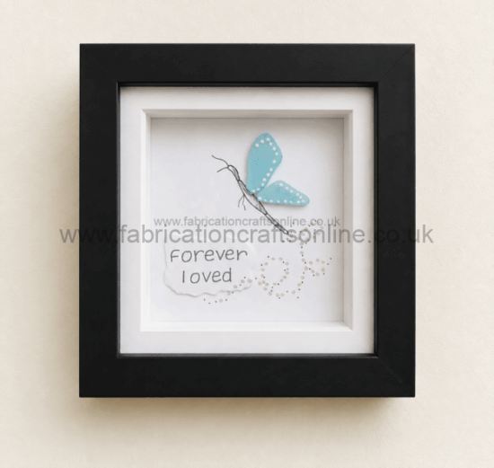 Framed artwork with a blue butterfly perched above the handwritten words ‘Forever I loved’ on white paper.