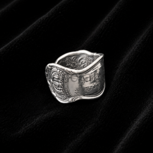 Ornate silver ring with floral engravings resting on black velvet surface