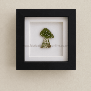 Framed artwork of a small green mushroom with a dotted cap and a floral-patterned stem, mounted on a white mat.