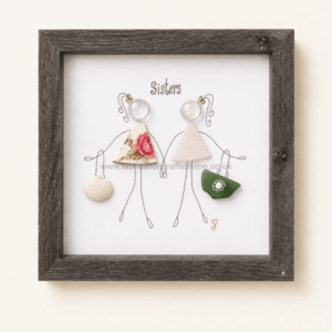 Framed illustration of two stick-figure sisters labeled 'Sisters'; each wears a fabric dress (floral and pink polka) and holds a shell and a green bag as accessories.