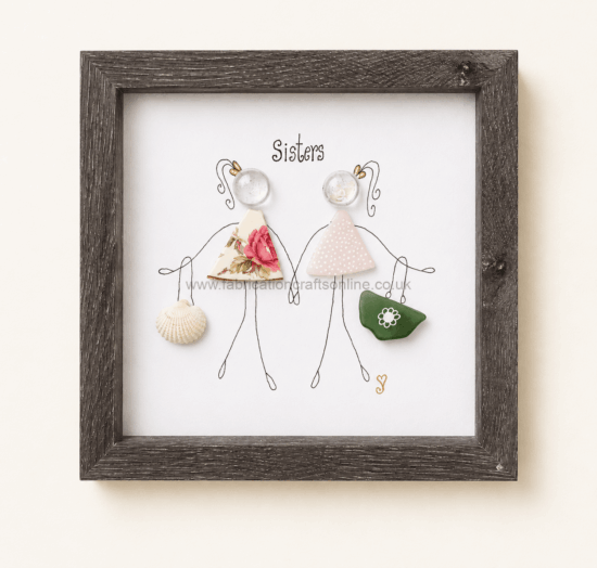 Framed illustration of two stick-figure sisters labeled 'Sisters'; each wears a fabric dress (floral and pink polka) and holds a shell and a green bag as accessories.