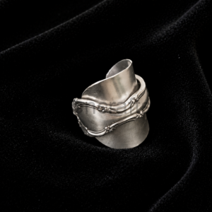 Close-up of a chunky silver ring with a decorative vine-like band resting on black velvet.