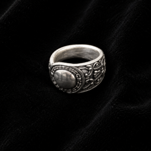 Silver ornate ring with filigree and a rounded bezel displayed on black velvet backdrop.