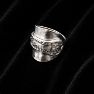 Silver wide-band ring with an engraved floral/scroll pattern resting on black velvet background.