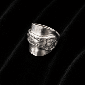 Silver wide-band ring with an engraved floral/scroll pattern resting on black velvet background.