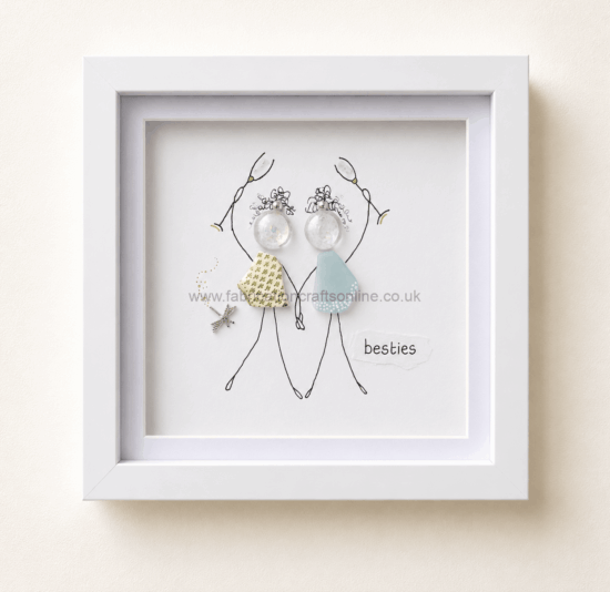 Framed illustration of two stick-figure friends holding hands, wearing fabric dresses, with decorative earrings and a star charm, captioned “besties”