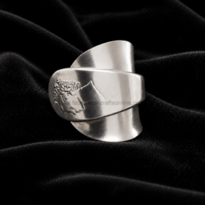 Wide silver cuff bracelet with a floral engraving resting on black velvet fabric