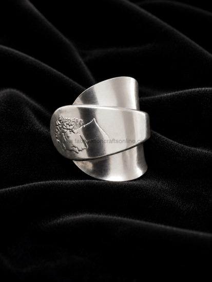 Wide silver cuff bracelet with a floral engraving resting on black velvet fabric