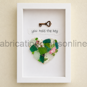 Framed art: a bronze heart-shaped key above a torn-paper caption 'you hold the key' with a mosaic heart of glass pieces.