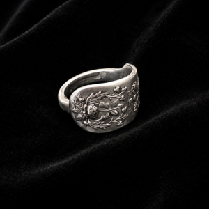 Silver ring with detailed floral relief on a black velvet background, close-up.