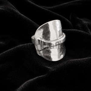 Wide silver statement ring with a hammered texture resting on black velvet fabric.