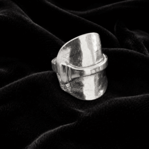 Wide silver statement ring with a hammered texture resting on black velvet fabric.