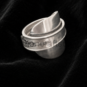 Silver metal napkin ring with a floral engraving resting on black velvet fabric.