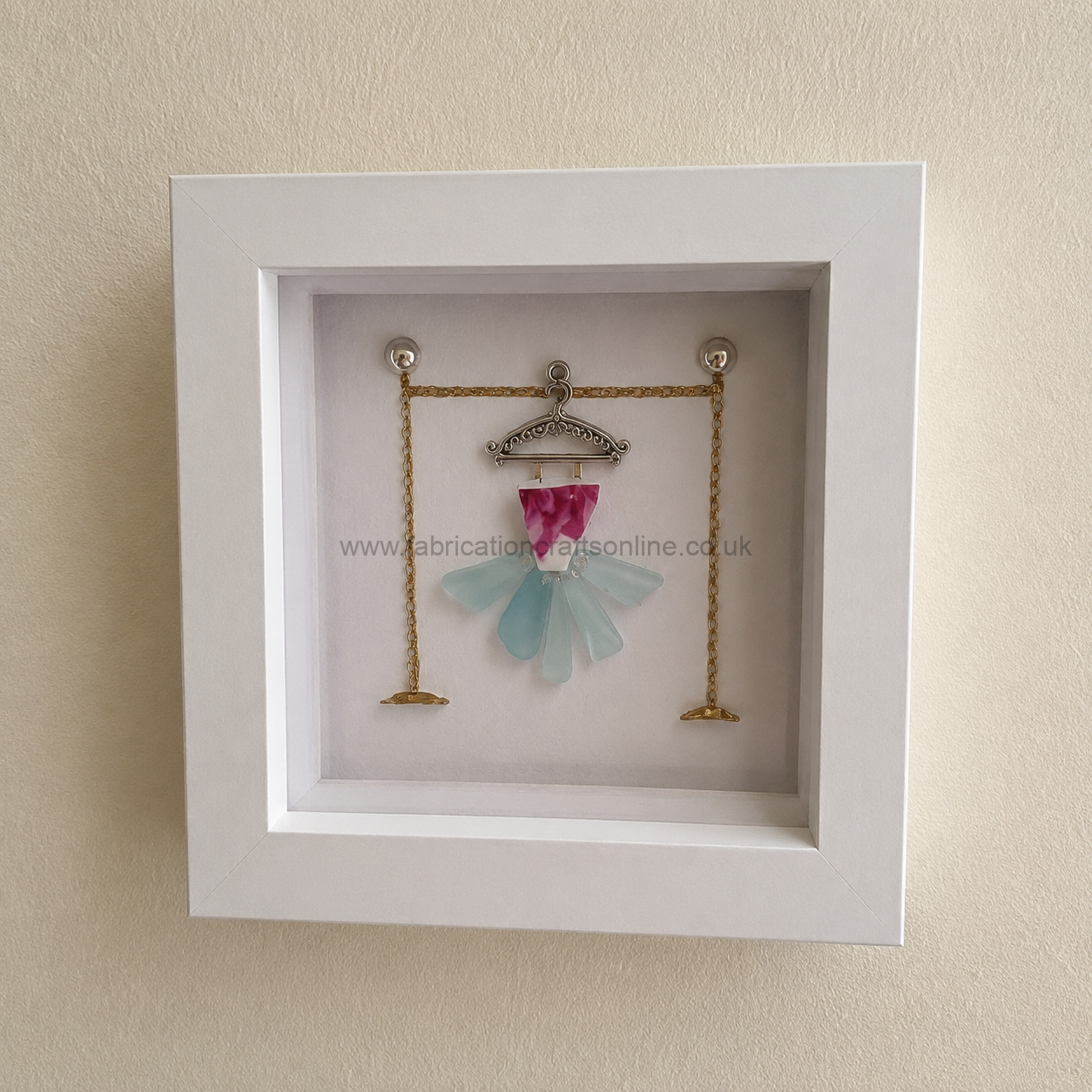 Sea Glass Art Dancer a charming handcrafted tutu dress made from genuine sea glass and vintage china hanging from an ornate coat hanger above a hand drawn display stand beautifully presented in a x cm white shadow box frame