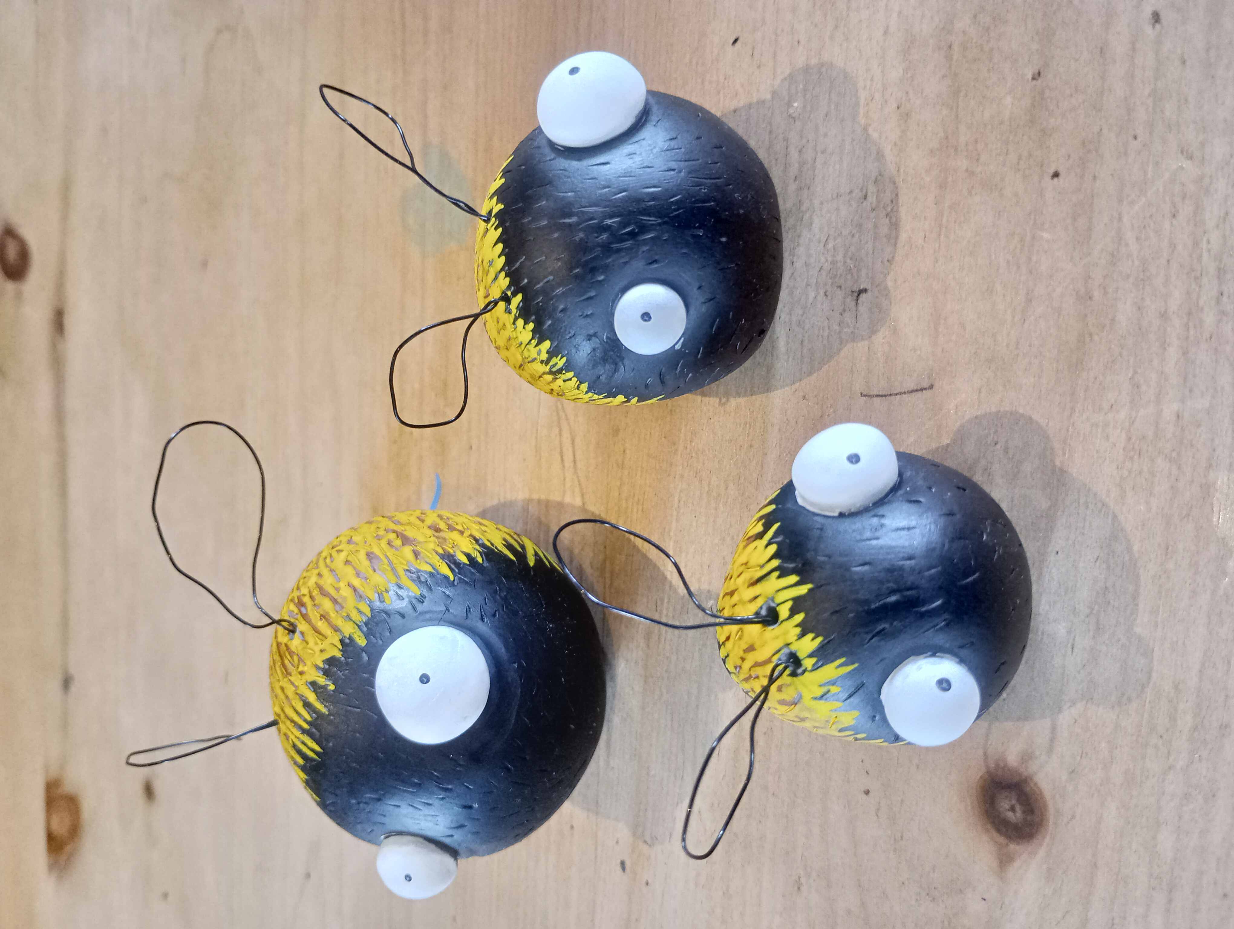 Beige wooden table with several handmade black-and-yellow bee-like craft balls, each with white eyes and metal wire antennae.