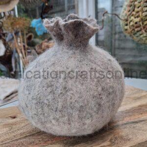 A round, light-gray felted decorative bag with a gathered top sitting on a wooden board, craft items in the background.