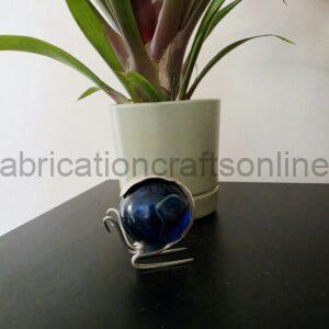 Green houseplant in a light ceramic pot on a dark table, with a blue glass decorative orb on a metal stand in front.