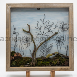 Framed botanical wire sculpture with plant shapes rising from mossy ground inside a wood frame, labeled Botanical Wireworks on the bottom corner.