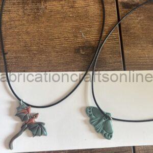 Two black cord necklaces on a white surface: left pendant is a small red and teal dragon with wings, right pendant is a teal butterfly.