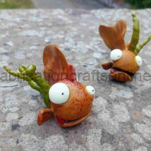 Two orange clay monster figurines with large white eyes sit on a rough stone surface outdoors.