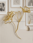 Gold wire sculpture of two abstract flowers resting on a light sofa surface.